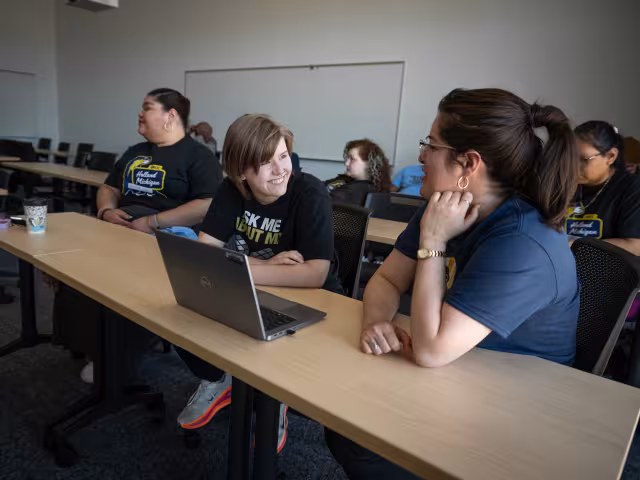 Two students sit at a laptop, talking