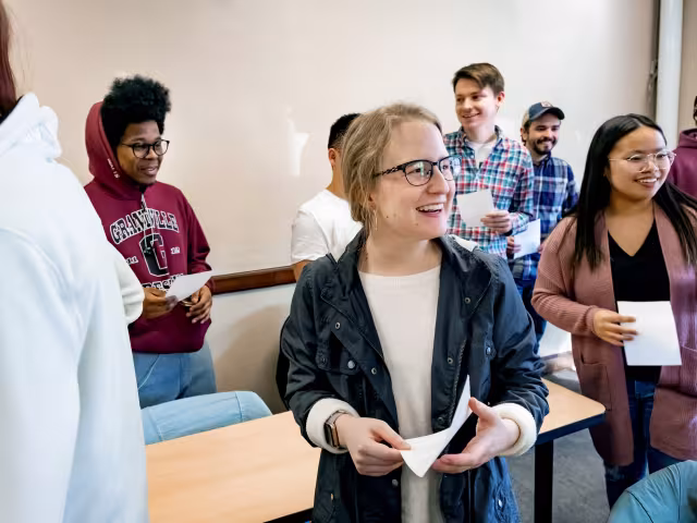 Students standing in a classroom, smiling.