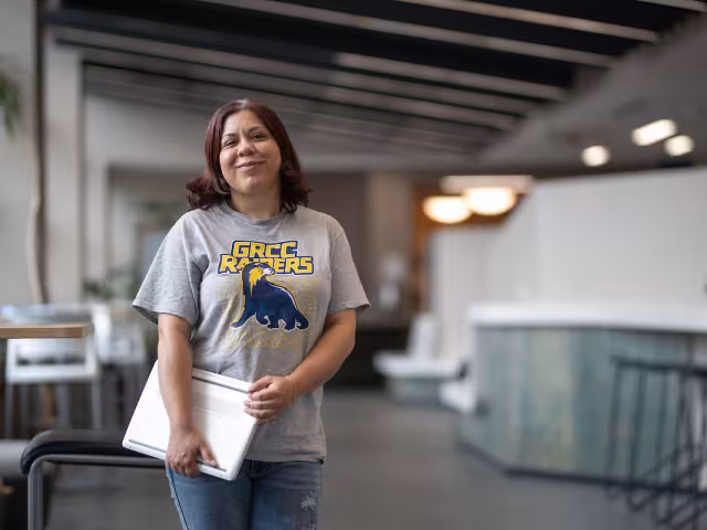 GRCC student wearing a Raiders shirt holds a laptop.